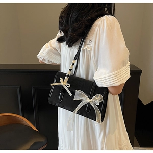 Detail of glossy black shoulder bag featuring layered woven and tulle bow decorations