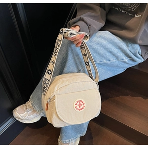 Close-up of beige nylon square crossbody bag with branded wide jacquard strap on a model
