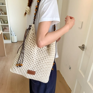 Close-up of beige crochet tote bag with wooden beads and brown leather logo tag