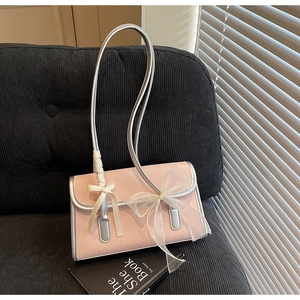 Detailed shot of pink textured shoulder bag with a large white tulle bow on dark corduroy