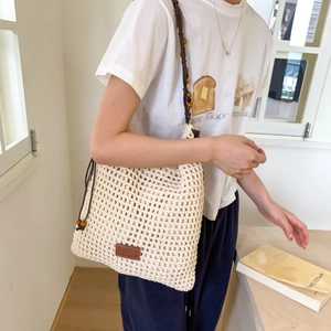 Detail of hollow woven shoulder bag with beaded straps and leather logo patch