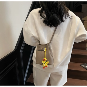 Crossbody view of taupe lychee texture bucket bag with a cute yellow duck charm detail