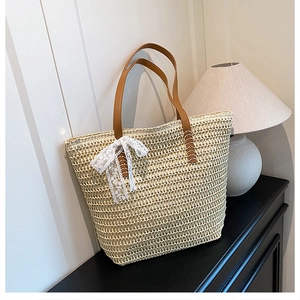 Detail of hand-woven straw tote bag featuring white lace bow and brown leather handles