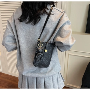 Detail of black crossbody phone bag with embossed bear pattern and cute teddy charm