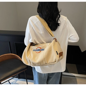 Vue détaillée du sac bandoulière en toile beige avec broderie logo bleue sur le côté