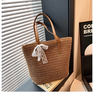 Detail of handwoven straw tote bag featuring a white lace bow and brown leather handles