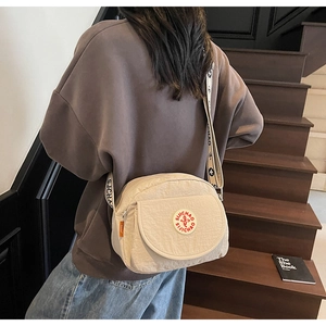Close-up of cream textured nylon crossbody bag with brand logo and jacquard strap