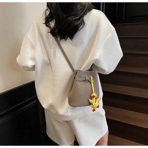 Detail of grey lychee leather bucket bag with cute yellow duck charm on a model