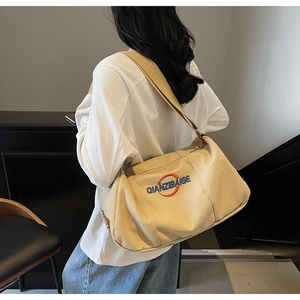 Détail d'un sac bandoulière en toile beige avec large sangle et logo brodé élégant