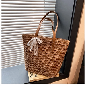 Close-up of woven straw tote bag with white lace bow and brown leather handles