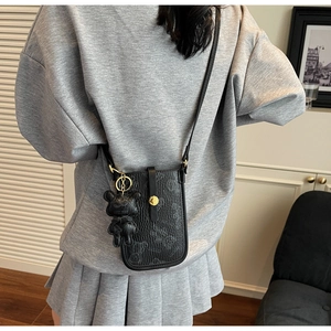 Close-up of black crossbody phone bag with teddy bear charm and embossed bear pattern