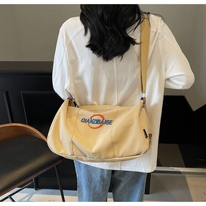 Détail du sac à épaule en toile beige avec broderie porté par le mannequin