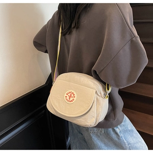Close-up of beige square crossbody bag with logo patch on model in daily setting
