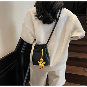 Detail of black leather bucket bag featuring a playful yellow duck charm on the strap