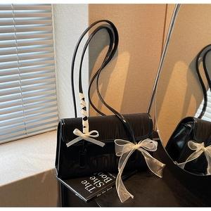 Close-up of glossy black shoulder bag with textured surface and white organza bow detail