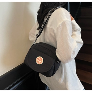 Detail of black nylon shoulder bag showing round embroidered logo and wide woven strap