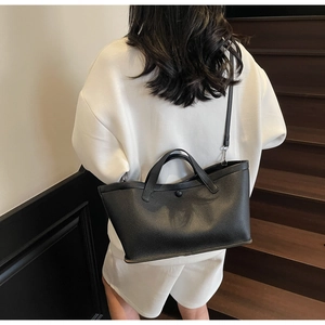 Close-up of black lychee grain leather tote bag with reinforced handles and crossbody strap