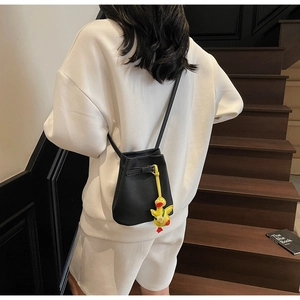 Detail view of a black lychee leather bucket bag with a yellow duck charm on a shoulder strap