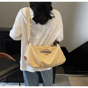 Détail du sac bandoulière en toile beige avec broderie bleue et large sangle en tissu