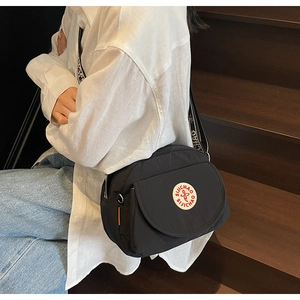 Detail of black crossbody bag with adjustable wide strap and white circular logo on front