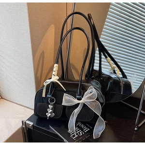 Close-up of black saddle bag featuring white organza bow and silver heart pendant detail