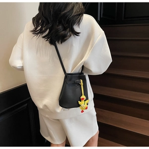 Detail of black lychee grain bucket bag featuring a cute yellow duck charm on shoulder strap