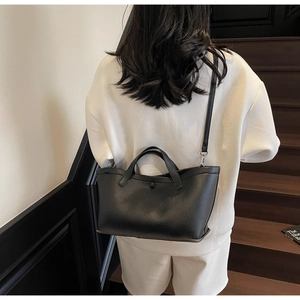 Close-up of black lychee grain leather tote bag with dual handles and detachable strap