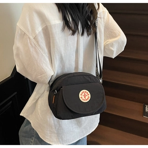 Detail view of black canvas crossbody bag with branded logo patch and wide letter strap