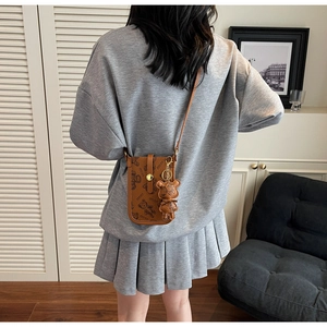 Detailed back view of a brown leather crossbody bag with cartoon bear patterns and a bear charm