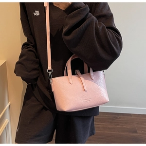 Side view of a light pink crocodile texture handbag worn by a model in a warm setting