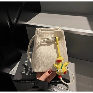 Detail of cream white bucket bag in lychee texture leather with a yellow duck charm