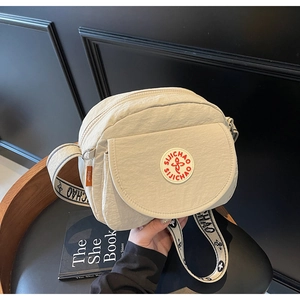 Close-up of off-white nylon crossbody bag with wide jacquard strap on a dark leather chair