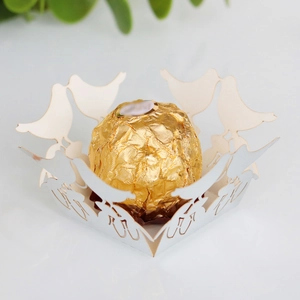 Macro detail of laser-cut white paper bird candy box with gold chocolate ball