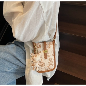 Detailed view of cream leather crossbody phone bag with teddy bear pattern and charm