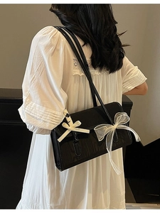 Fashionable black underarm bag with white bows and glossy leather shown with a model