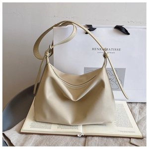 Detail of minimalist beige hobo bag with adjustable strap placed on an open book