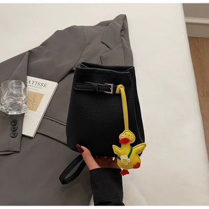 Close-up of black lychee grain bucket bag with cute yellow duck charm and metal buckle detail