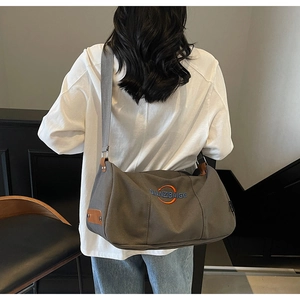 Détail d'un sac bandoulière en toile grise avec broderie et accents en cuir