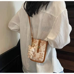 Detail of crossbody phone bag featuring teddy bear print and plush charm on a model