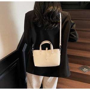 Close-up of a cream pebbled leather handbag worn with a black blazer on a wooden staircase