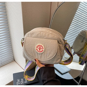 Detail of light beige nylon crossbody bag with colorful woven shoulder strap and logo patch