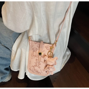 Close-up of pink crossbody bag with teddy bear print and matching charm on a model
