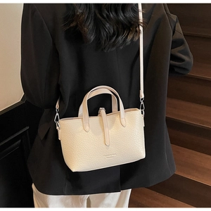 Detail view of a creamy white leather handbag with litchi texture and adjustable strap