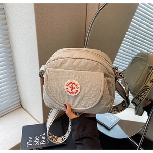 Detail of a beige nylon crossbody bag with circular red logo and wide branded strap