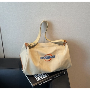 Détail du sac boston en toile beige avec logo brodé et bandoulière en tissu réglable