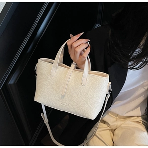 Detail of cream crocodile textured square handbag with sturdy handles and logo