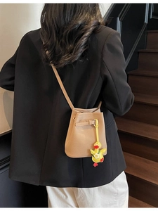 Beige lychee pattern bucket bag with yellow duck charm shown on model in black blazer