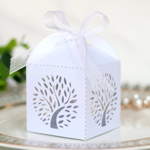 Laser-cut white wedding favor box with hollow tree design and ribbon on ceramic plate