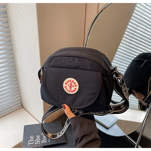 Detail of a casual black nylon crossbody bag with logo patch and wide branded strap