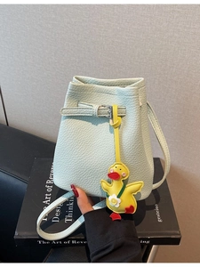 Mint green bucket bag with lychee texture and a yellow duck charm on an art book